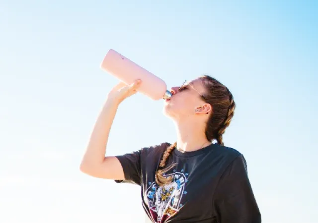 写真:青空の元水筒から水を飲む女性